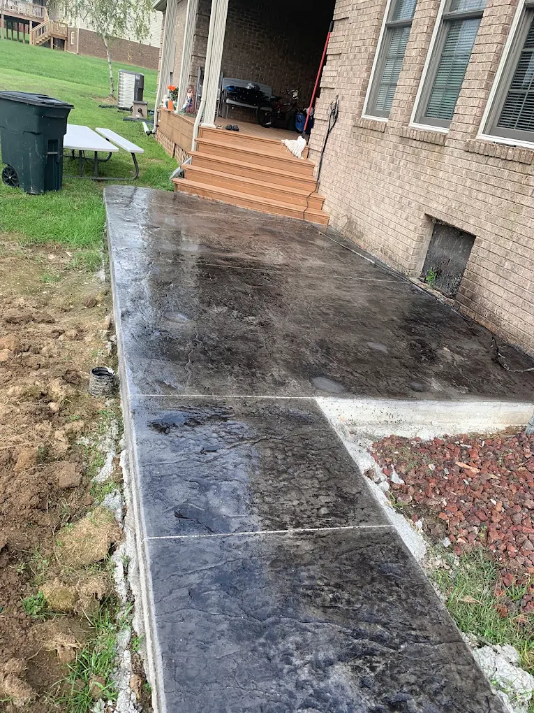 Dark stamped concrete walkway beside red rock landscaping