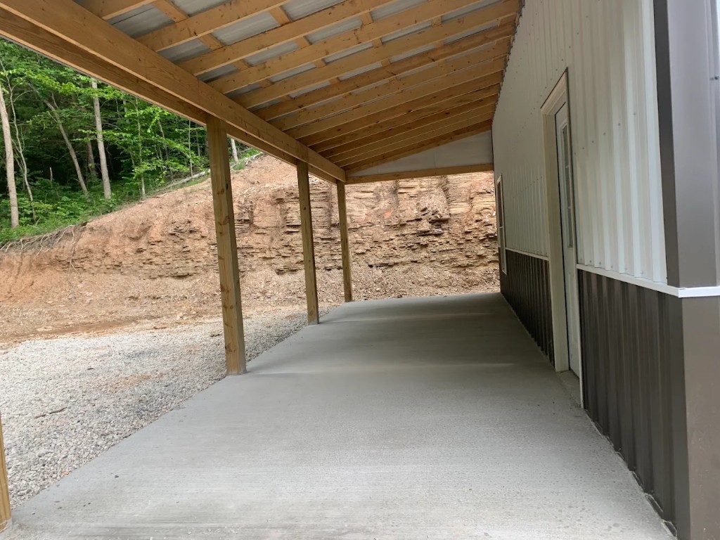 Concrete porch slab poured under a timber roof on a metal-sided building
